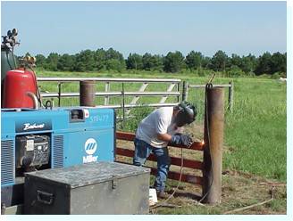 Man welding a gate with a welding mask on standing beside his equipment