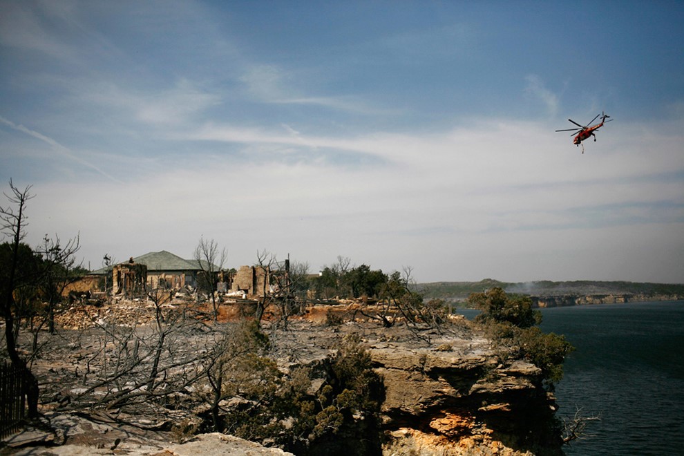 TWO HOUSES SURROUNDED BY ASHES FROM A WILDFIRE. ONE HOME IS BURNT DOWN, WHILE THE OTHER REMAINS STANDING